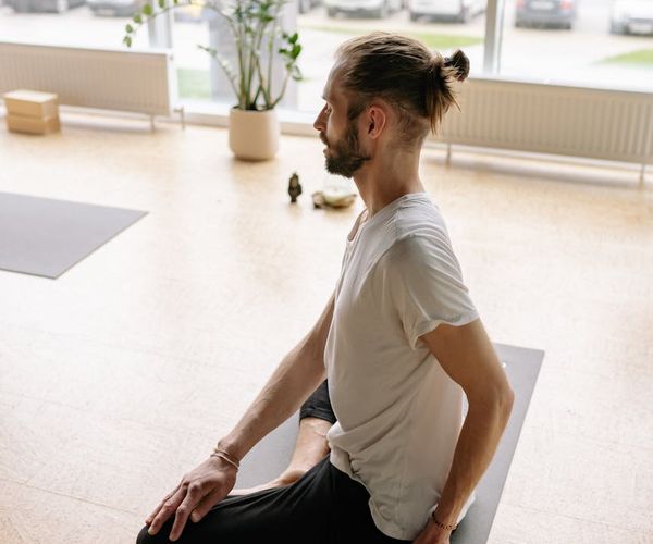 A serene person sitting in a meditative yoga pose by a large window.